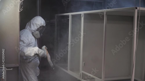 Man painting with spray paint gun in workshop. Clip. Industrial metal coating. Man in protective suit, wearing a gas. Professional factory worker paints metal with guns at manufacture automatic powder photo
