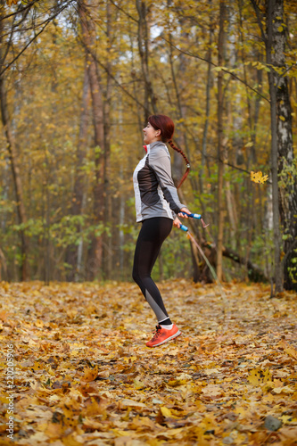 Full-length picture of young brunette jumping with rope at autumn forest