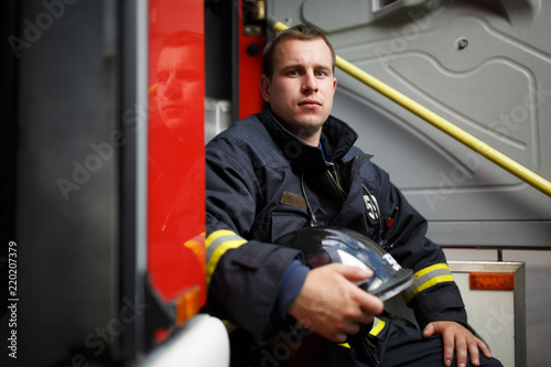 Photo of fireman with helmet in hands sitting in fire engine