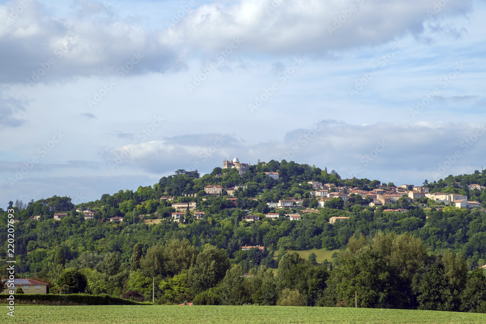 Early summer view across fields to hilltop Penne d'Agenais and Notre-Dame de Peyragude basilica with its silver dome, Lot et Garonne, France.