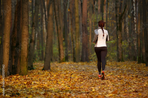 Image from back of young sports girl in running through forest