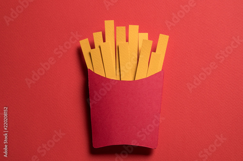 French fries in red package on red paper background. Scrapbooking, paper cut style image for fast food cafe or restaurant. Concept of fast food, fat, calories, unhealthy nutrition.