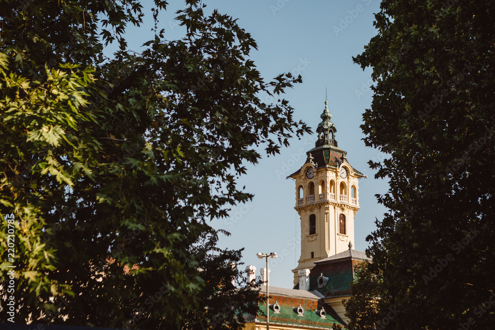Tower of City Hall between the park treesk in Szeged in south Hungary during the sunny summer day with the blue sky in background