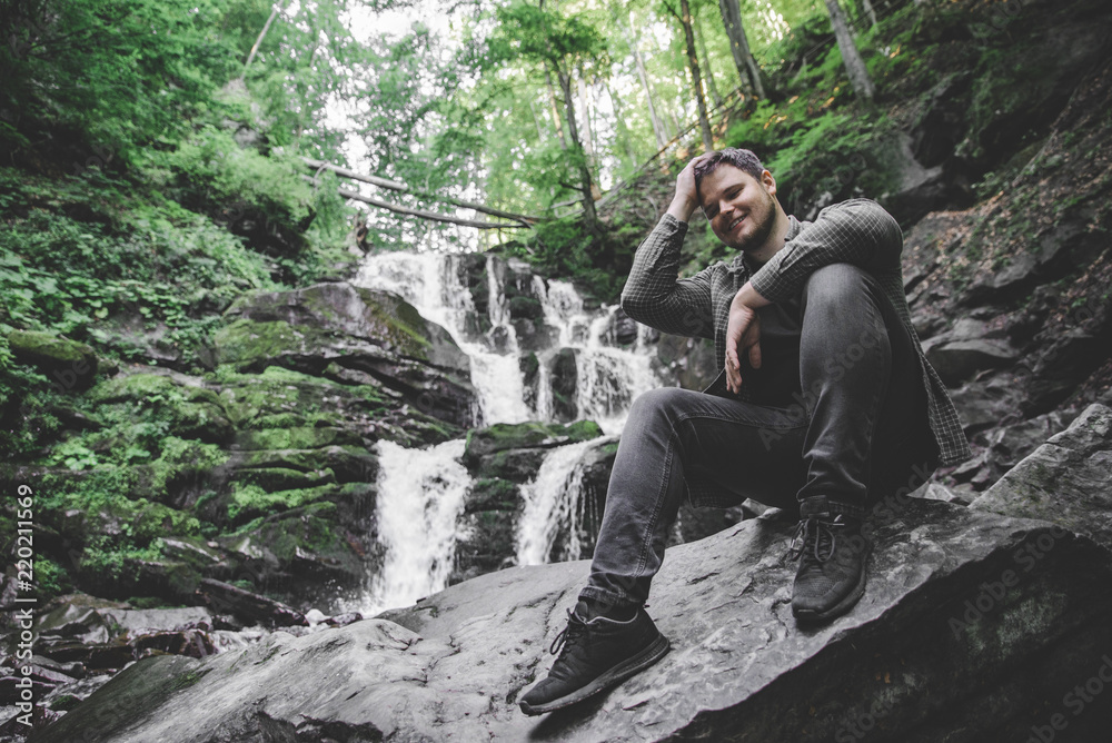 man sitting at rock with waterfall on background man sitting at rock with waterfall on background