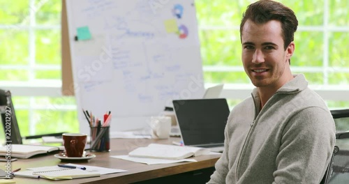 Young and handsome Caucasian businesman sitting on desk and looking stare at camera with self-confident manner in modern office. Concept for lifestyle of working man.
