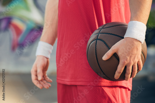 cropped image of basketball player in red sportswear holding basketball ball on street © LIGHTFIELD STUDIOS