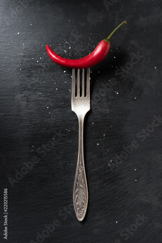top view of red ripe chili pepper and fork on black surface