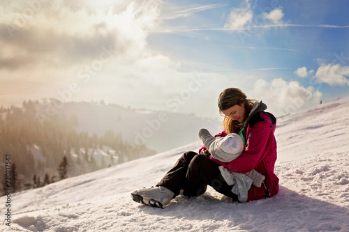 Young mother, breastfeeding her baby boy on top of mountain on sunset in Austrian Alps
