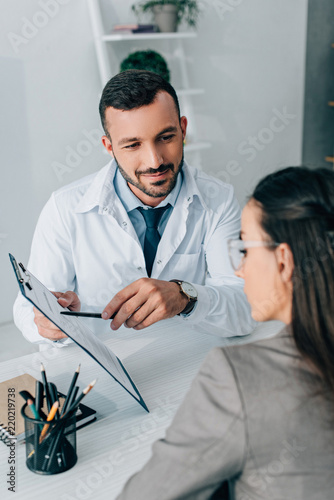 Fotografie cheerful doctor pointing on insurance claim form to patient in clinic