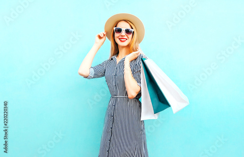 Fashion portrait smiling woman with shopping bags in striped dress, summer round straw hat on blue background