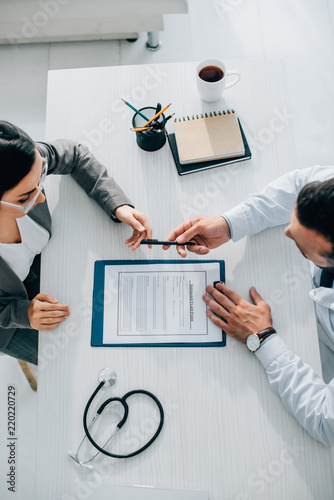 Fotografie high angle view of doctor giving pen to patient to sign insurance claim form in