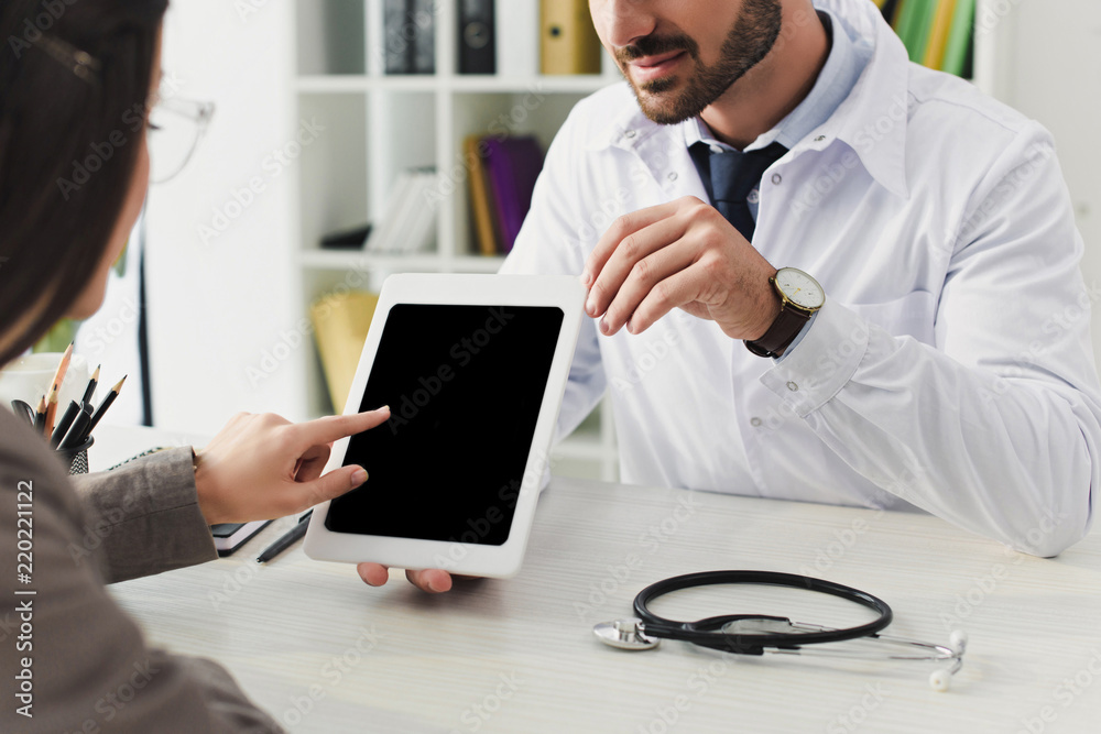 cropped image of doctor showing patient tablet with blank screen in clinic cropped image of doctor showing patient tablet with blank screen in clinic