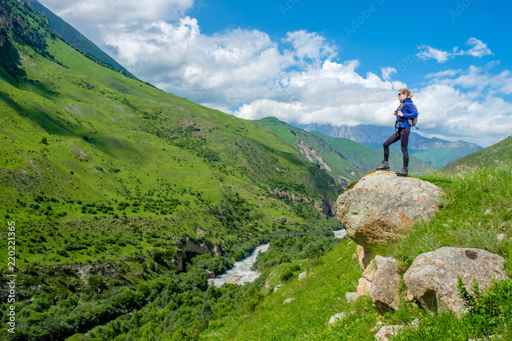 A girl with a backpack is resting in the mountains. Panorama of the Caucasus Mountains.