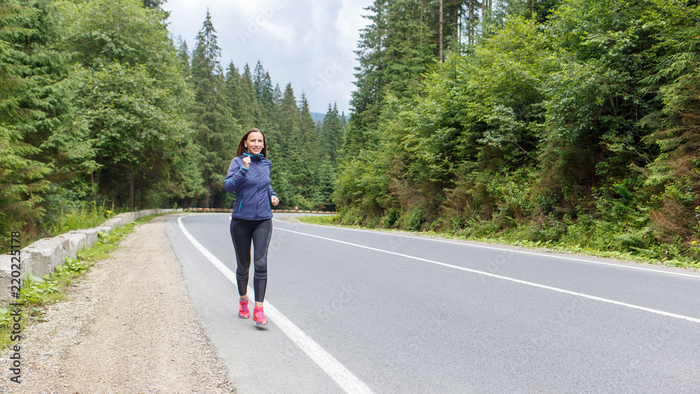Young smiling woman jogging on mountain road. Happy girl with long hair running in mountains in autumn. Healthy lifestyle background with copy space Young smiling woman jogging on mountain road. Happy girl with long hair running in mountains in autumn. Healthy lifestyle background with copy space