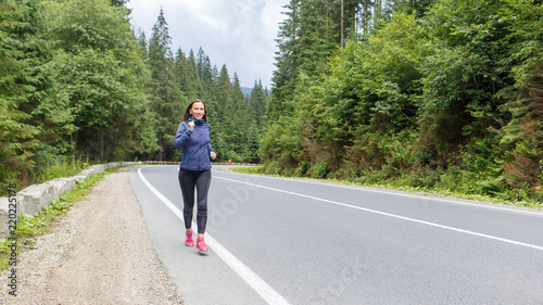 Young smiling woman jogging on mountain road. Happy girl with long hair running in mountains in autumn. Healthy lifestyle background with copy space