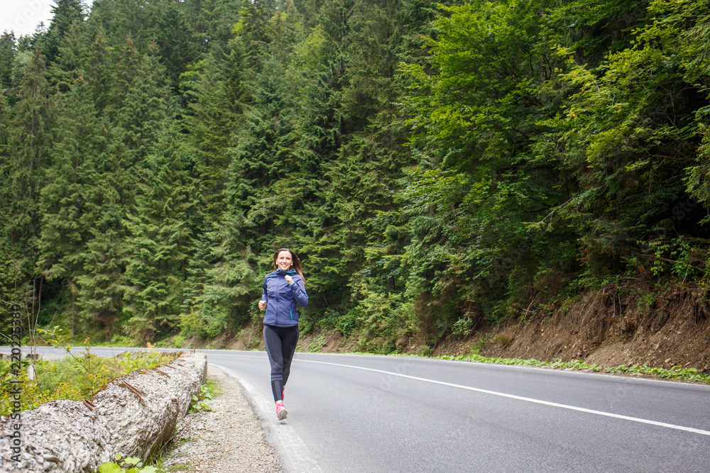 Obraz premium Young smiling woman jogging on mountain road. Happy girl with long hair running in mountains in autumn. Healthy lifestyle background with copy space