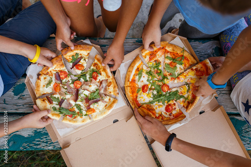 Top view image of children grab slices of pizza from box at the outdoors picnic. Children hands taking pizza