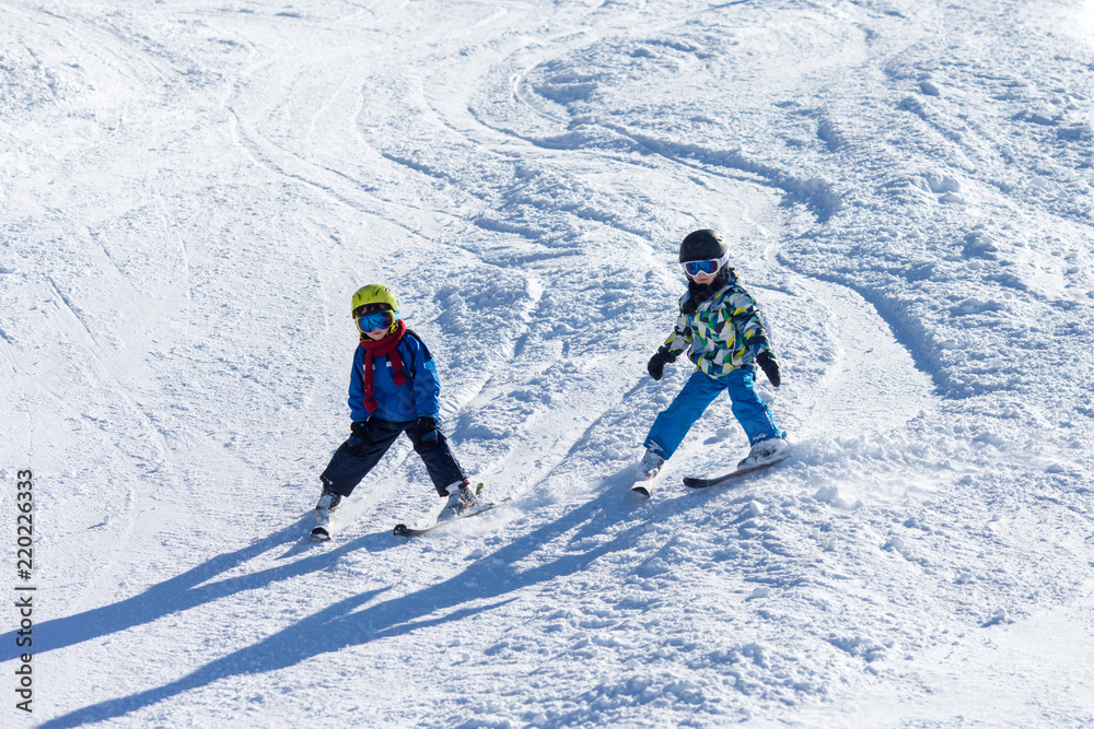 Two young children, siblings brothers, skiing in Austrian mountains on a sunny day