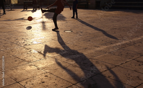Shadows of people playing in football in a street of the city at the sunset
