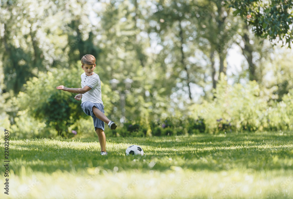 full length view of happy boy playing with soccer ball on grass in park