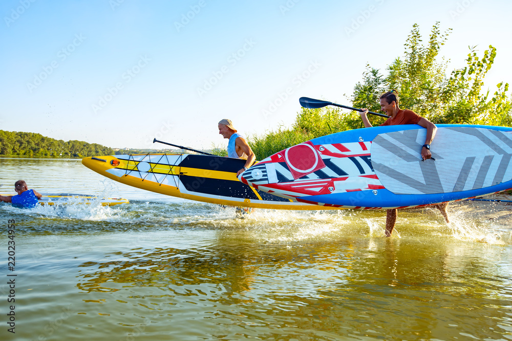 Joyful friends with SUP boards in their hands are running to the water