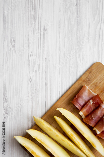 Melon slices with prosciutto on bamboo board over white wooden background, top view. Overhead, flat lay, from above. Space for text.