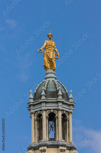 Edinburgh  Scotland  UK - June 14  2012  Golden statue of female representing Victory on top of tower of the Mound building against blue sky. Seen from Royal Mile.
