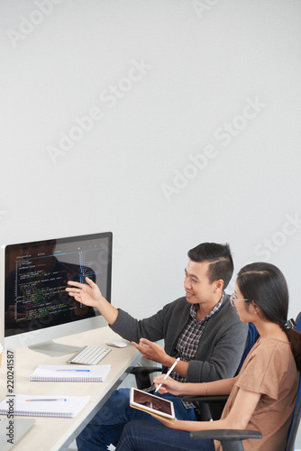 Asian software developers discussing code on computer screen