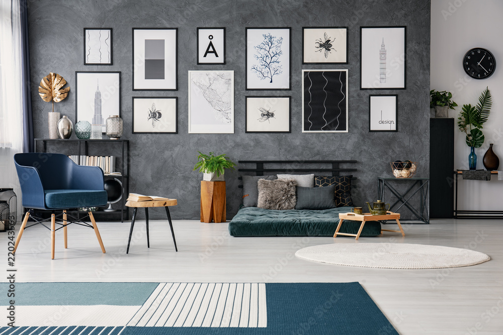 Fototapeta Carpet in grey spacious flat interior with blue armchair next to table near green futon. Real photo