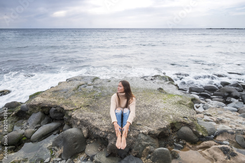 lonely beautiful young woman listen music and relaxing with meditation and concentration sitting on a rock with ocean and horizon and nobody in background. enjoying loneliness concept