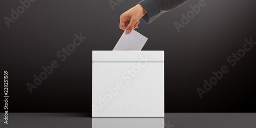 Fotografie Hand inserting an envelope in a white blank ballot box on black background, copy space