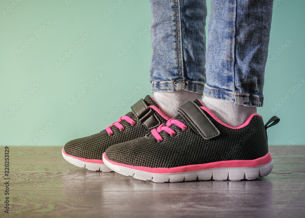 The girl's legs in torn jeans and black and red sneakers on the wooden floor  near the blue wall. Stock Photo | Adobe Stock