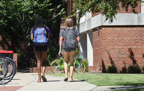 Fotografie 2 female college students wearing shorts walk across campus on a hot summer day