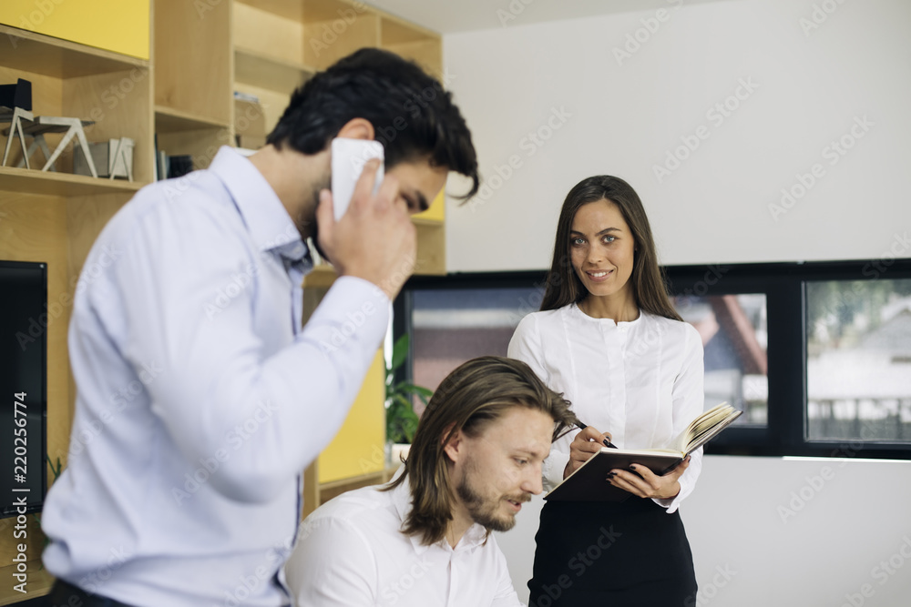 Handsome businessman using mobile phone in the office while other business people sitting in background Handsome businessman using mobile phone in the office while other business people sitting in background