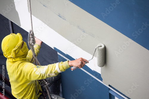 painters hanging on roll, painting color on building wall. facade builder worker with roller brush, working on high building. safety construction with lift rope belt in city. 