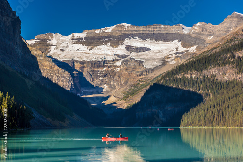 Fototapeta Naklejka Na Ścianę i Meble -  Banff, Canada - Ago 19th 2017 - Tourists doing kayak and enjoying the amazing scenario of lake Moraine, early morning light, glacial at the background, blue sky in summer time Banff.