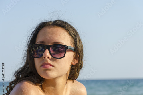beautiful young woman with glassess and bikini seriously sitting on beach