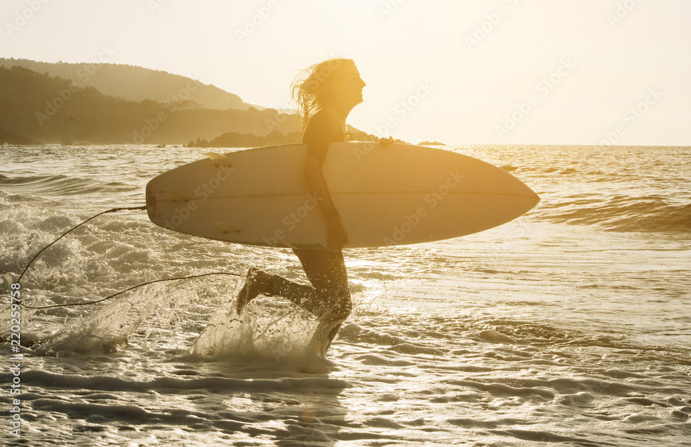 Woman with surfboard standing on wet sandy beach at the ocean.