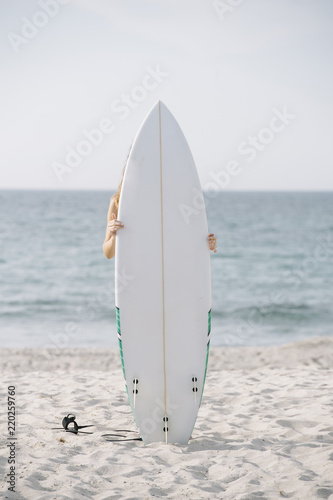 Anonymous person hugging while surfboard while standing on background of waving sea