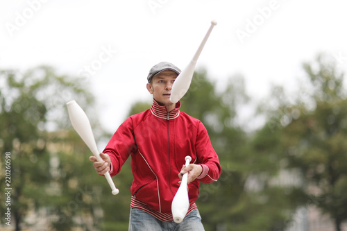 A man in a cap juggles with clubs on the street of a European city