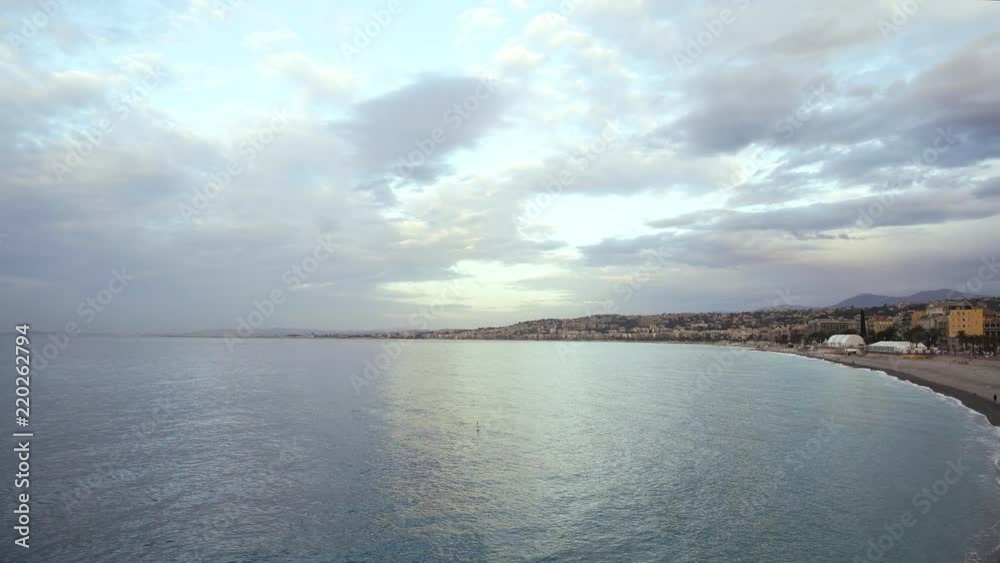 Sunrise on a cloudy spring day on the coast of French Nice. People walking in warm clothes. Vehicles driving in the background. Concept of tourism. Left to right pan real time establishing shot Sunrise on a cloudy spring day on the coast of French Nice. People walking in warm clothes. Vehicles driving in the background. Concept of tourism. Left to right pan real time establishing shot