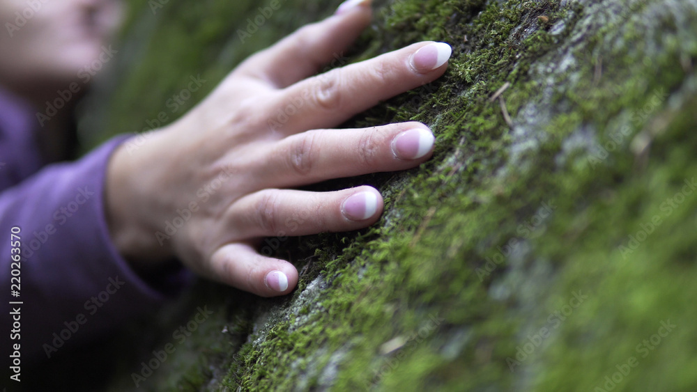 Hugging a nature. A woman puts her arms around large stone with moss, exchanging emotions and charging energy from nature.