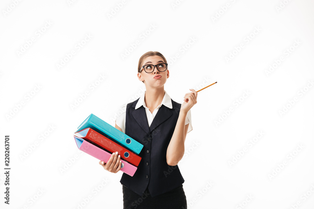 Young woman in black vest and eyeglasses thoughtfully looking up holding colorful folders and pencil in hands over white background isolated Young woman in black vest and eyeglasses thoughtfully looking up holding colorful folders and pencil in hands over white background isolated