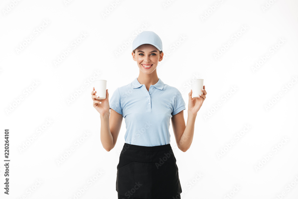 Beautiful smiling girl in blue polo T-shirt and cap holding in hands disposable cups for water while happily looking in camera over white background Beautiful smiling girl in blue polo T-shirt and cap holding in hands disposable cups for water while happily looking in camera over white background