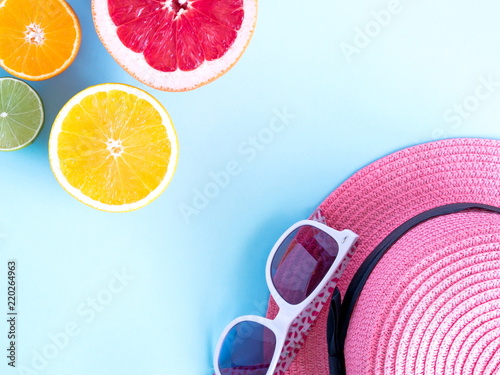 Creative background made of summer tropical fruits and pink straw hat. Grapefruit  orange  tangerine  lemon  lime on pastel light blue background.   oncept of travel and recreation. Flat lay  top view 
