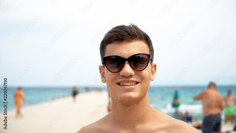 Happy smiling handsome young teen smile and correct his hairstyle and  sunglasses on beach, cinematic dof, summer holidays and people concept  Stock Photo | Adobe Stock