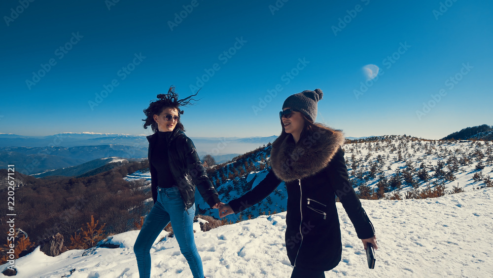 Two happy teen friends running on snow smiling, cinematic steadicam tracking shot
