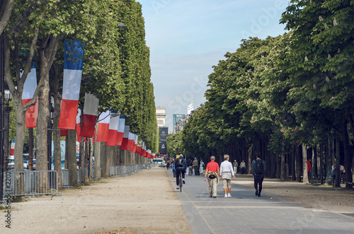 Paris, France - May 10, 2017: People walk down the Champs Elysees with French flags on trees waving celebrating national holliday in Paris, France