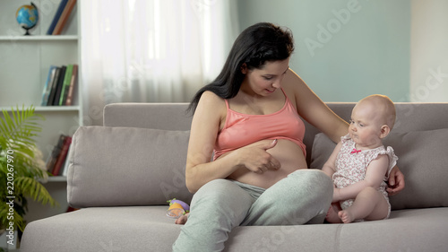 Woman enjoying pregnancy, touching her big belly and telling baby about sister