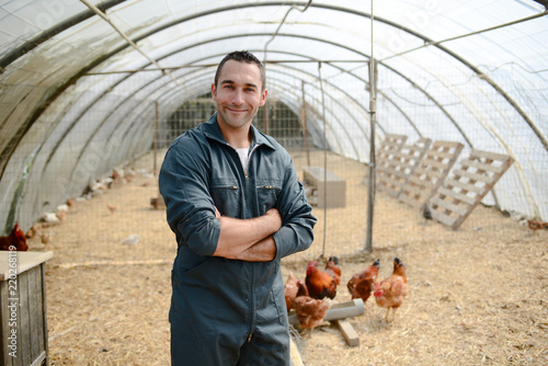 portrait of handsome young farmer veterinarian taking care of poultry in a small chicken farm photo